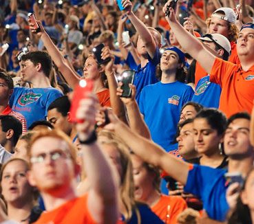 Gator fans cheering students holding phone light in the stadium