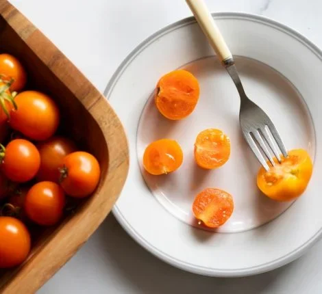 A plate with small tomatoes next to a basket of tomatoes.